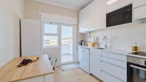 A modern kitchen with white cabinetry, a microwave, a dishwasher, and a wooden table with a fruit platter. - Serra&Rio no Sado - By Y Concept (Setúbal)