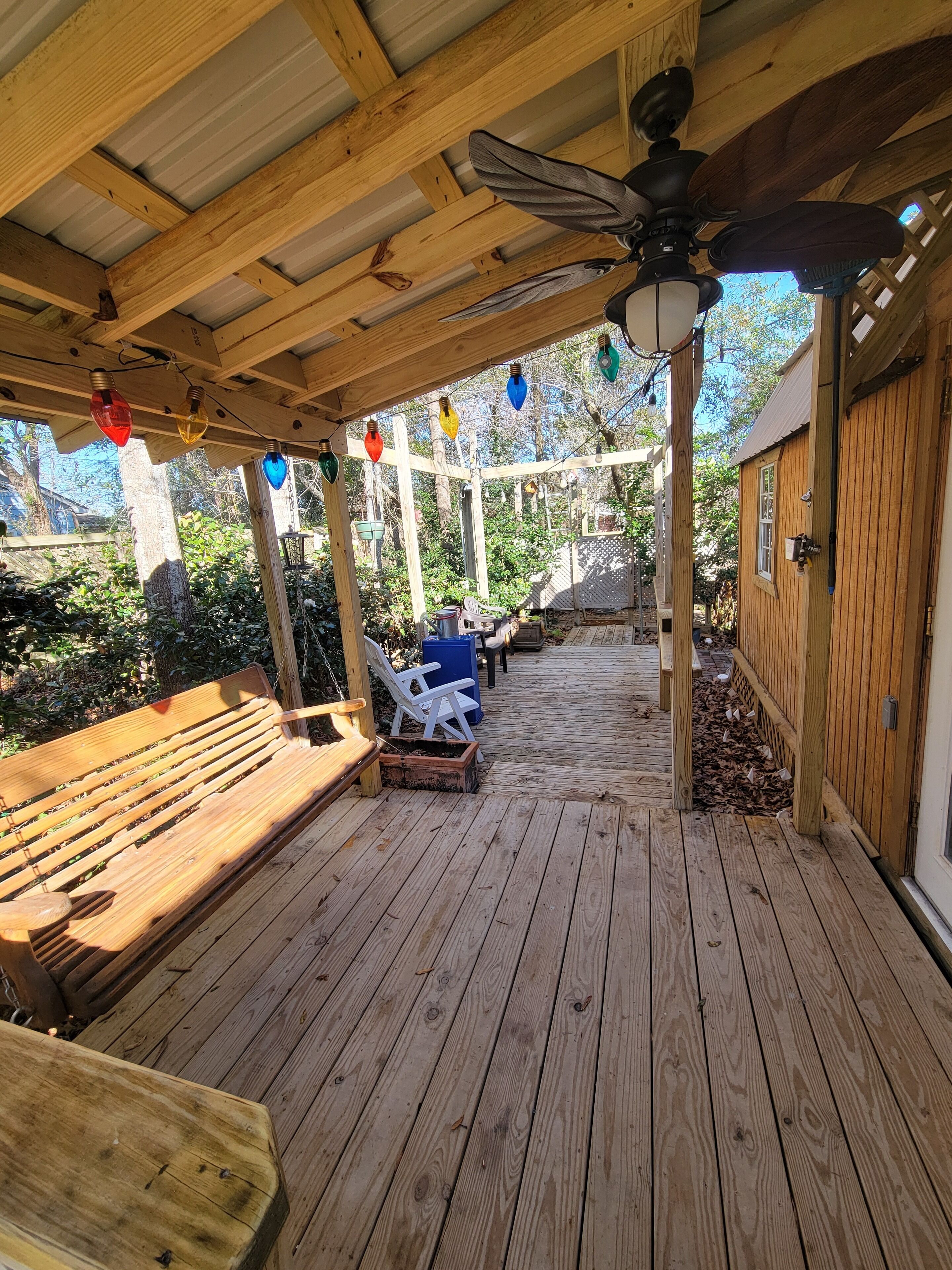 A wooden deck with a ceiling fan, a bench, and two lawn chairs.