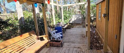 A wooden deck with a ceiling fan, a bench, and two lawn chairs.