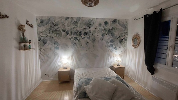 Une chambre à coucher comprenant un lit, deux tables de chevet avec des lampes, un miroir fixé au mur et une étagère décorative avec des plantes.