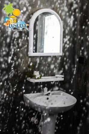 Un bagno con un lavandino bianco, uno specchio e un piccolo ripiano con un fiore.