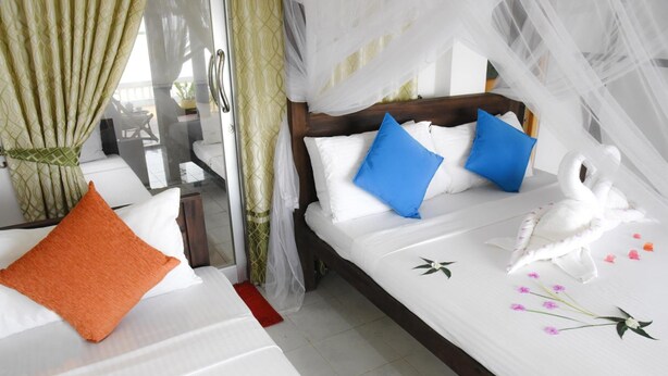 A hotel room with a bed, a window with curtains, and a decorative swan on the bed. - Dinuda Resort (Kudawa)