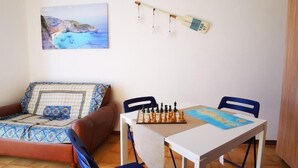 Una habitación con una cama, una mesa con un tablero de ajedrez y un cuadro que representa una escena costera.