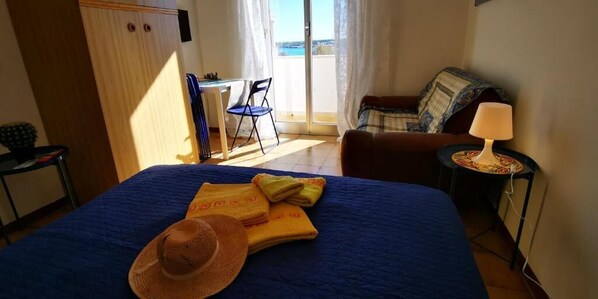 A bedroom with a bed, a desk, a chair, and a view of the outside.