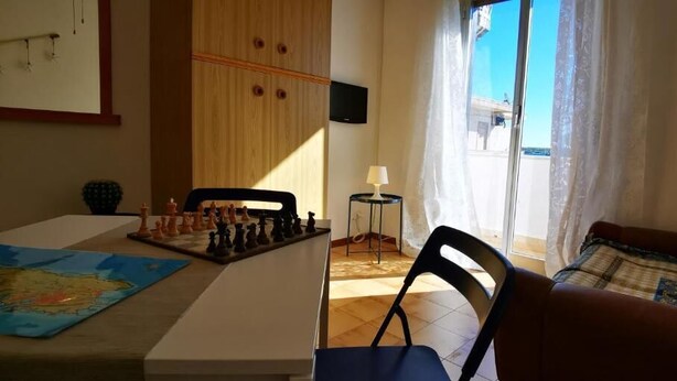 Una habitación con un tablero de ajedrez sobre una mesa, un sofá, un televisor en la pared y una ventana con cortinas.