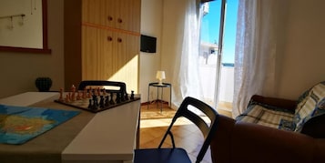 Una habitación con un tablero de ajedrez sobre una mesa, un sofá, un televisor en la pared y una ventana con cortinas.