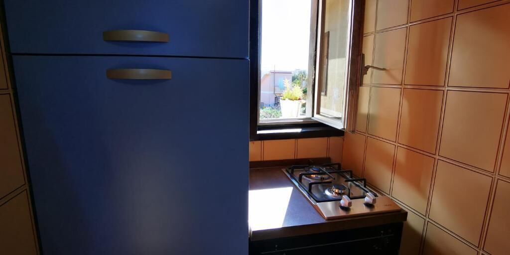 Une cuisine avec un meuble bleu, une cuisinière à gaz et une fenêtre donnant sur l’extérieur.