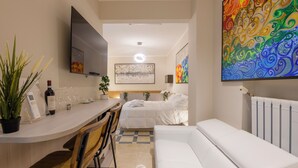 A modern hotel room with a bed, a sofa, a dining area with a table and chairs, a TV mounted on the wall, and a large abstract painting. - Dibra Luxury Suites (Milano)