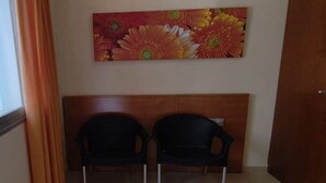 Una stanza con due sedie nere di fronte a una testiera in legno, un grande quadro floreale al muro e una porta in legno.