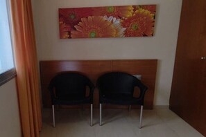 Ein Zimmer mit zwei schwarzen Stühlen vor einem Holz-Kopfteil, einem großen Blumenbild an der Wand und einer Holztür.