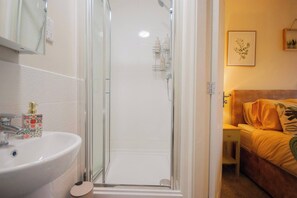 A bathroom with a glass shower enclosure, a white sink with a decorative soap dispenser, and a bed with a yellow blanket and a plant on the wall. - Luxe 3BR - 8 Min to Town Centre - Bradgate Park & Leicester - Parking - Garden (Loughborough)