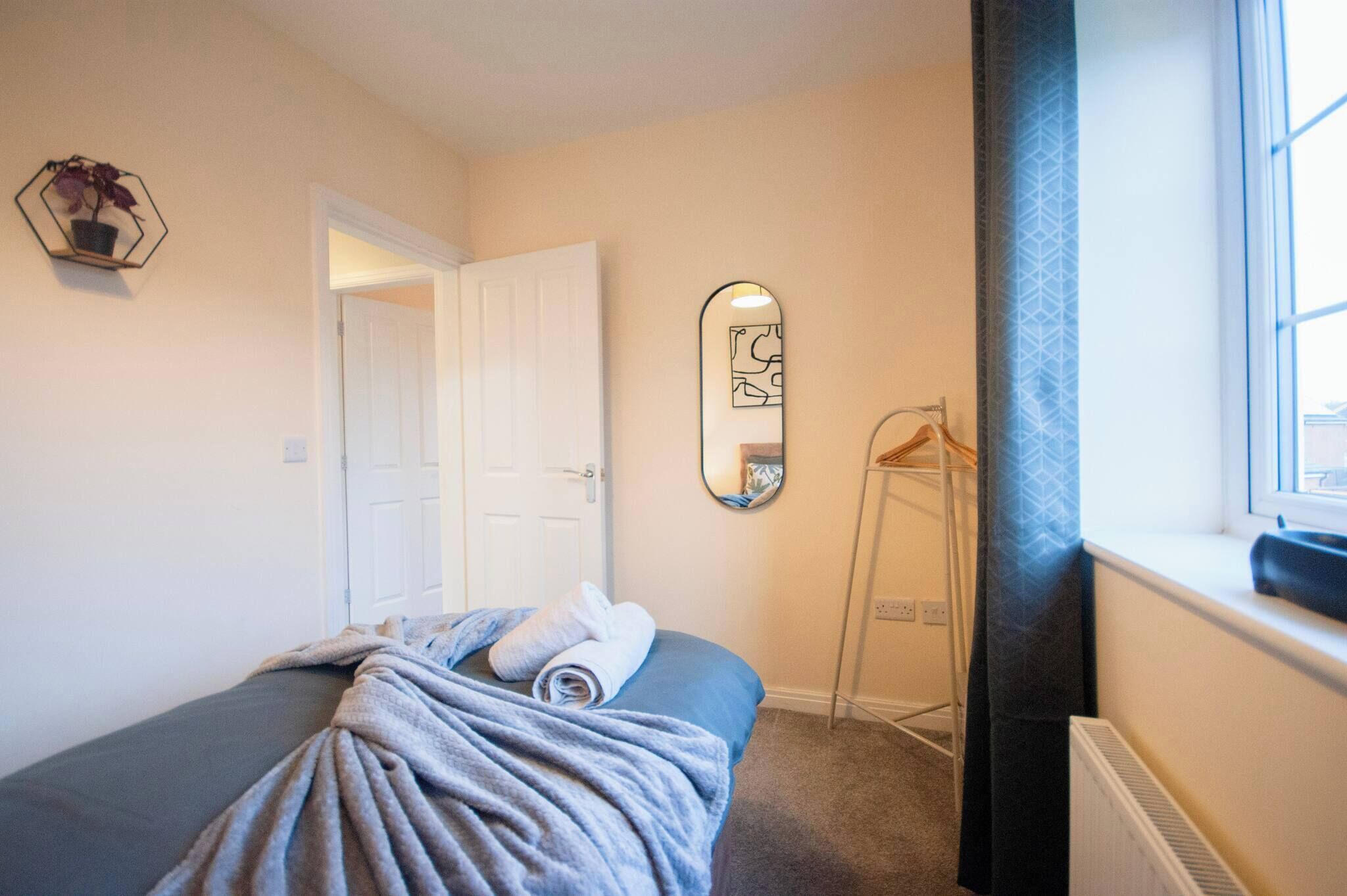 Un dormitorio con cama, perchero, espejo y puerta.