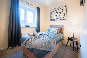 A bedroom with a bed, a window with curtains, a radiator, a wall art piece, and a bedside table with a lamp. - Luxe 3BR - 8 Min to Town Centre - Bradgate Park & Leicester - Parking - Garden (Loughborough)