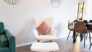 A modern dining area with a white upholstered chair with gold legs, a green armchair, and a dining table set with plates, glasses, and a vase of flowers. - Luxe 3BR - 8 Min to Town Centre - Bradgate Park & Leicester - Parking - Garden (Loughborough)
