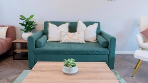 A teal sofa with floral cushions, a small potted plant on a wooden table, and a white chair with gold legs. - Luxe 3BR - 8 Min to Town Centre - Bradgate Park & Leicester - Parking - Garden (Loughborough)