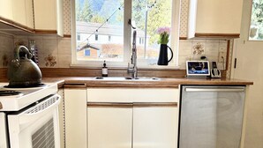 Une cuisine avec une fenêtre, une bouilloire, un évier, une cuisinière et un lave-vaisselle.