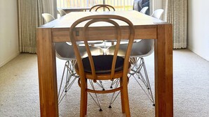 Un espace repas avec une table et des chaises en bois, un lustre et une vue sur un quartier résidentiel par le biais d’une grande fenêtre.