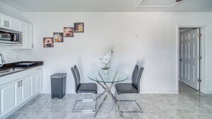 Eine moderne Küche mit weißen Schränken, einer Mikrowelle und einem Essbereich mit einem Glastisch und zwei Stühlen.