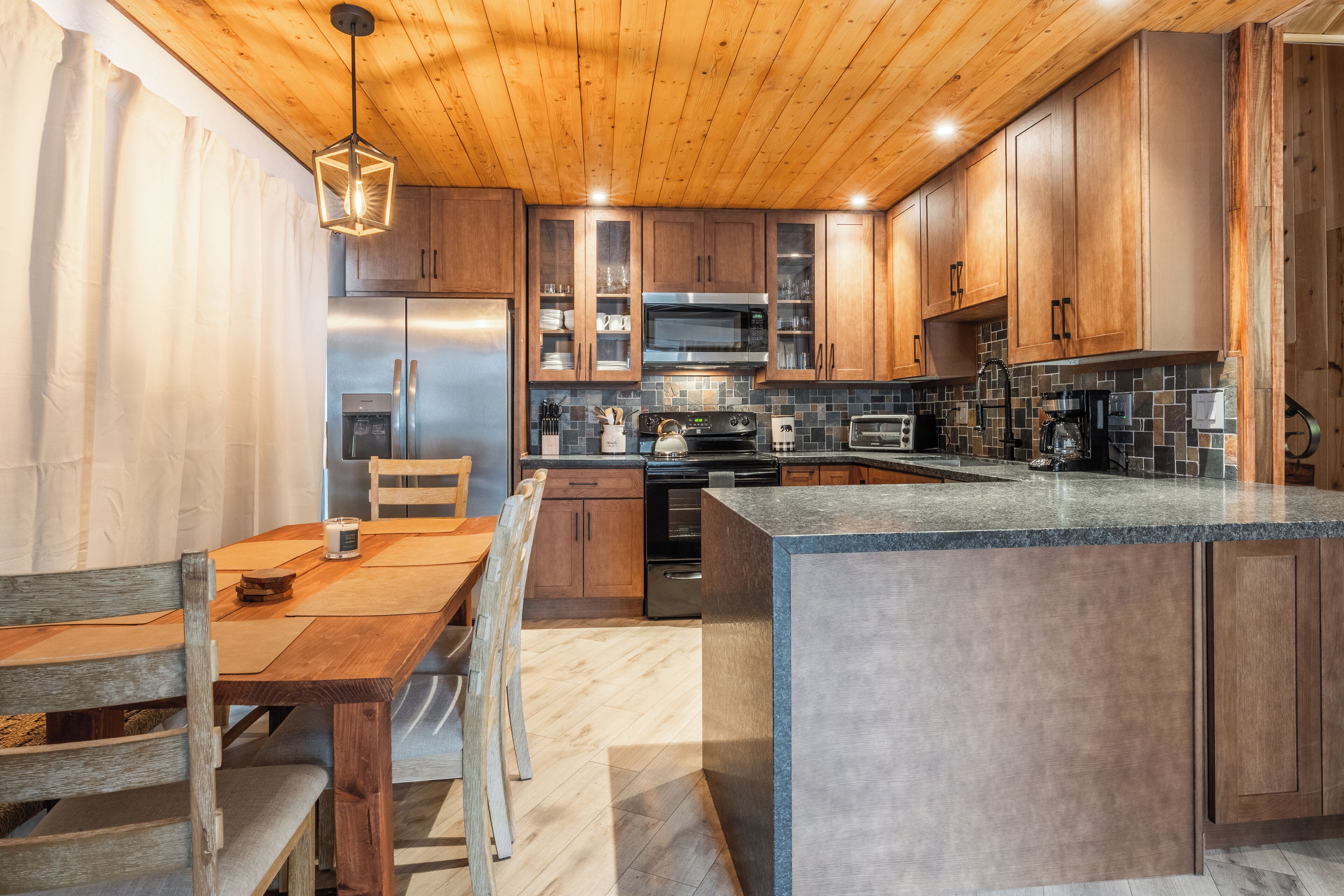 Une cuisine moderne avec des meubles en bois, un îlot central, des appareils électroménagers en acier inoxydable et un luminaire suspendu.