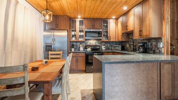 Une cuisine moderne avec des meubles en bois, un îlot central, des appareils électroménagers en acier inoxydable et un luminaire suspendu.