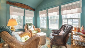 Una habitación acogedora con mobiliario de mimbre, un aparador de madera con cristalería y ventanas grandes con cortinas blancas.