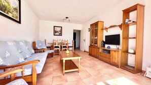 A living room with a sofa, dining table, chairs, a TV, and wooden cabinets. - Son Bepa , (Cales Piques)