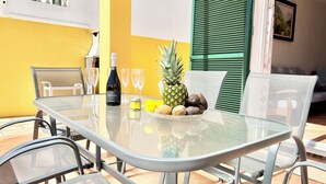 A glass-top table with a bottle of wine, two glasses, a pineapple, and a bowl of fruits. - Son Bepa , (Cales Piques)