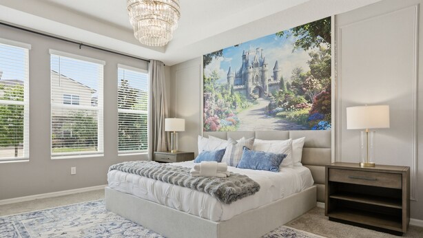 Ein Schlafzimmer mit einem großen Bett, zwei Nachttischen, einer Chandelüstere und einem großen Fenster mit Jalousien.