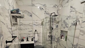 Een badkamer met marmeren wanden, een houten vloer, een douchecabine van glas, een zwarte wastafel en een wit toilet.