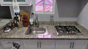 Een keuken met witte kastjes, een granieten aanrecht, een gasfornuis, een spoelbak en een raam met uitzicht op gebouwen.
