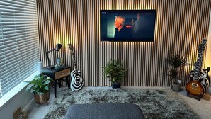Una sala de estar con televisor montado en una pared a rayas, una guitarra y una planta en maceta.