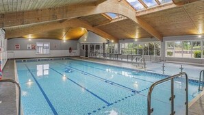 Una piscina interior con marcas de carriles claras, techo de madera y vistas al exterior a través de amplios ventanales.