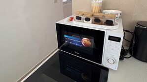 Een keuken met een magnetron en oven, een raam en een prullenbak.