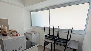Een compacte keuken met een magnetron, een kleine koelkast en een raam met jaloezieën.