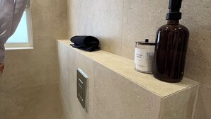 Een badkamer met beige tegels, een douchegordijn, een zwarte handdoek, een flesje wattenbolletjes en een pompflacon.