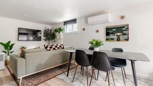 Een moderne woonkamer met een grijze bank, zwarte stoelen, een eettafel en een grote spiegel.