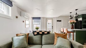 Een moderne woonkamer met een groene bank, een geruit plaid en uitzicht op de keuken.