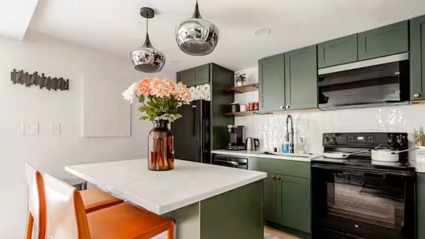 Een moderne keuken met groene kastjes, een witte aanrechtblad en een zwarte oven. Op het eiland staat een vaas met bloemen.