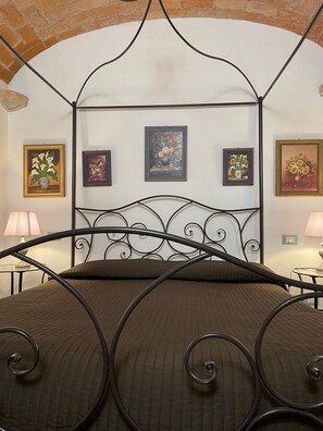 A room with a metal four-poster bed, a brick wall, and three framed floral paintings on the wall. - Città Giardino B&B - Un'oasi di tranquillità vicino la metro Conca d'Oro (Roma)