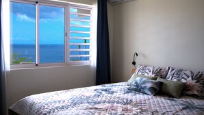 A bedroom with a bed, a window with blinds, an air conditioning unit, and a view of the sea. - Romantic 1BR with Ocean View, Salt Pans with Flamingos and Infinity Pool (Curacao)