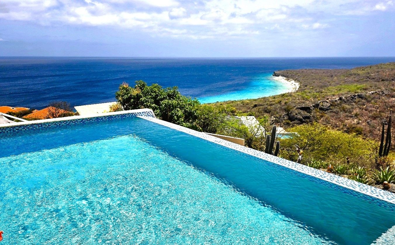 A clear blue pool with a view of the ocean and a rocky landscape.