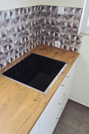 Eine Küche mit Holzarbeitsplatte, einer schwarzen Induktionskochplatte und einer Spritzschutzwand mit geometrischem Muster.