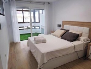 Ein Schlafzimmer mit einem Bett, einem Nachttisch, einem Fenster mit Vorhängen und Blick auf ein Gebäude.