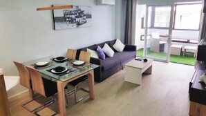 Una sala de estar moderna con una mesa de comedor de vidrio, un sofá oscuro y un gran ventanal corredizo que da a un área exterior.