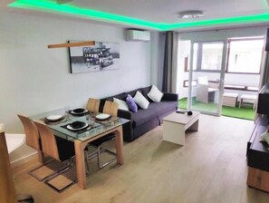 Ein modernes Wohnzimmer mit einem Glastisch, einer dunkelgrauen Couch und einer Schiebetür zum Außenbereich.