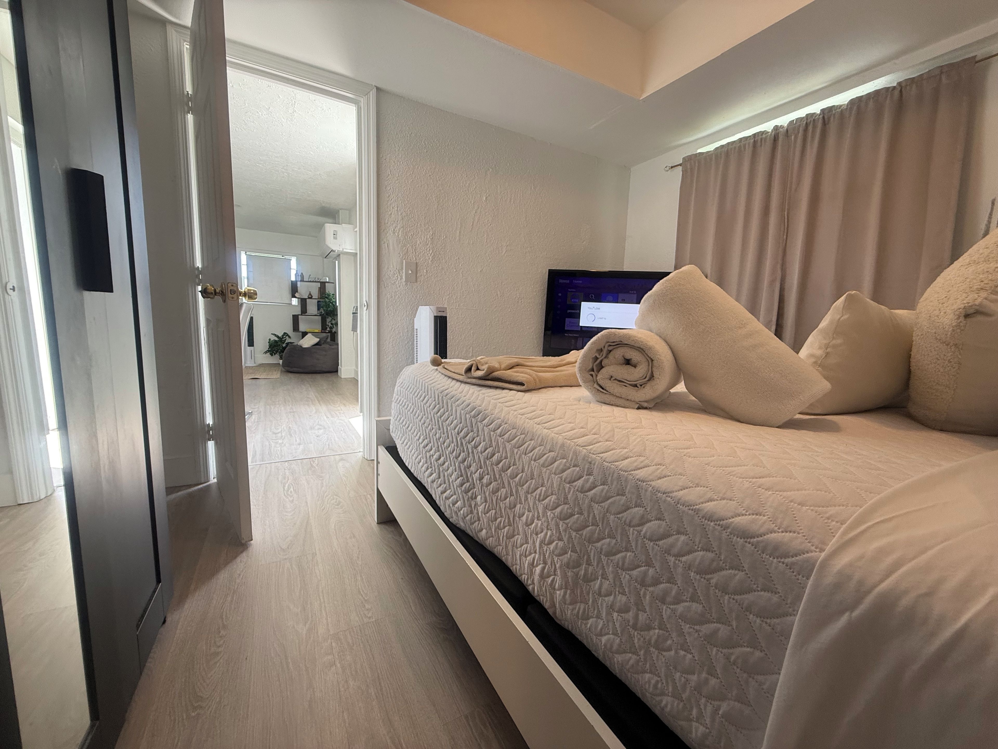 Habitación de hotel con cama, almohadas, televisor y vista al área de estar.