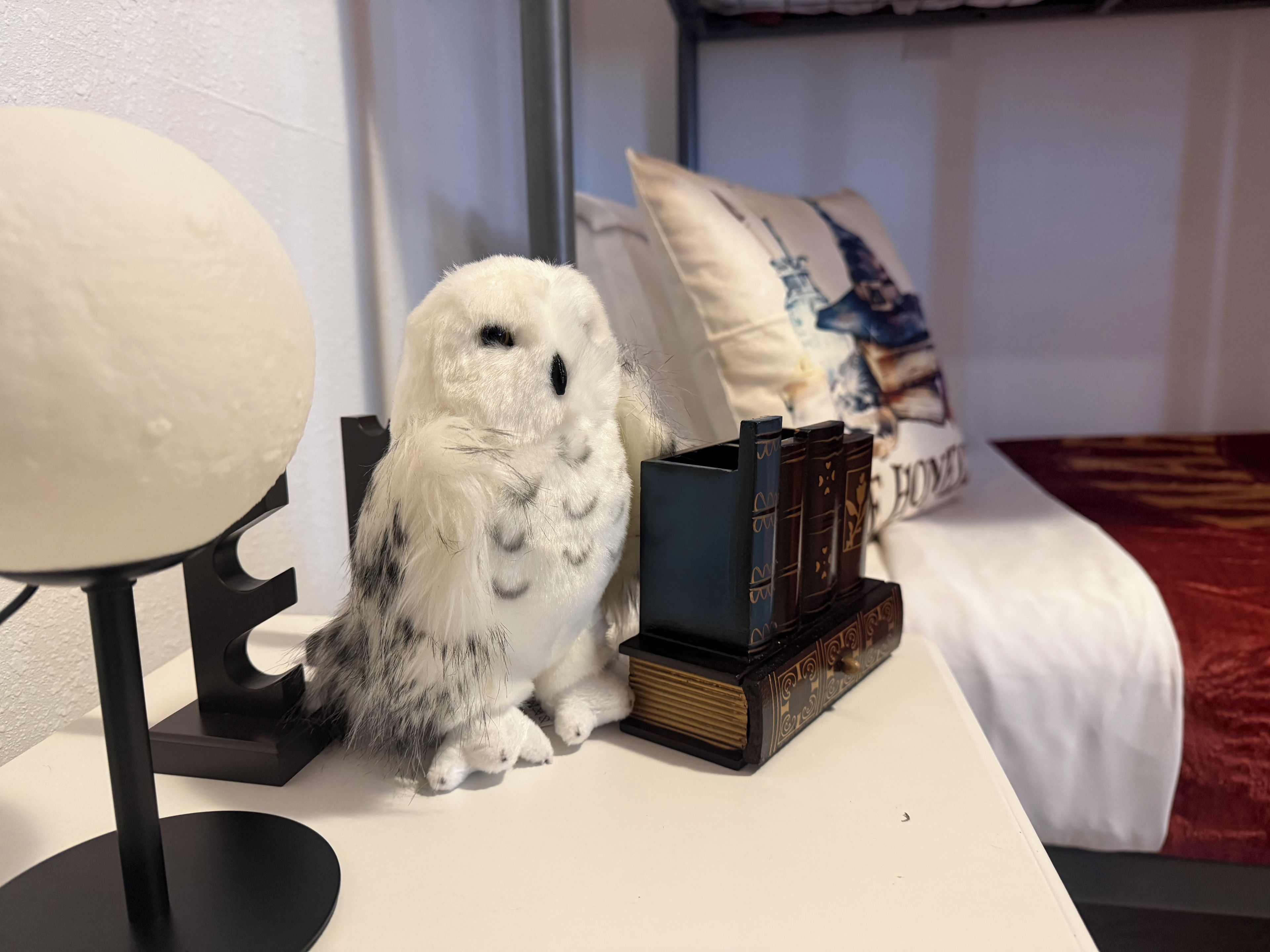 A white owl on a table with a lamp and books.