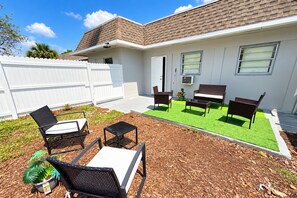 Una propiedad residencial con un área de patio que cuenta con mobiliario exterior, una mesita y una jardinera con césped artificial.