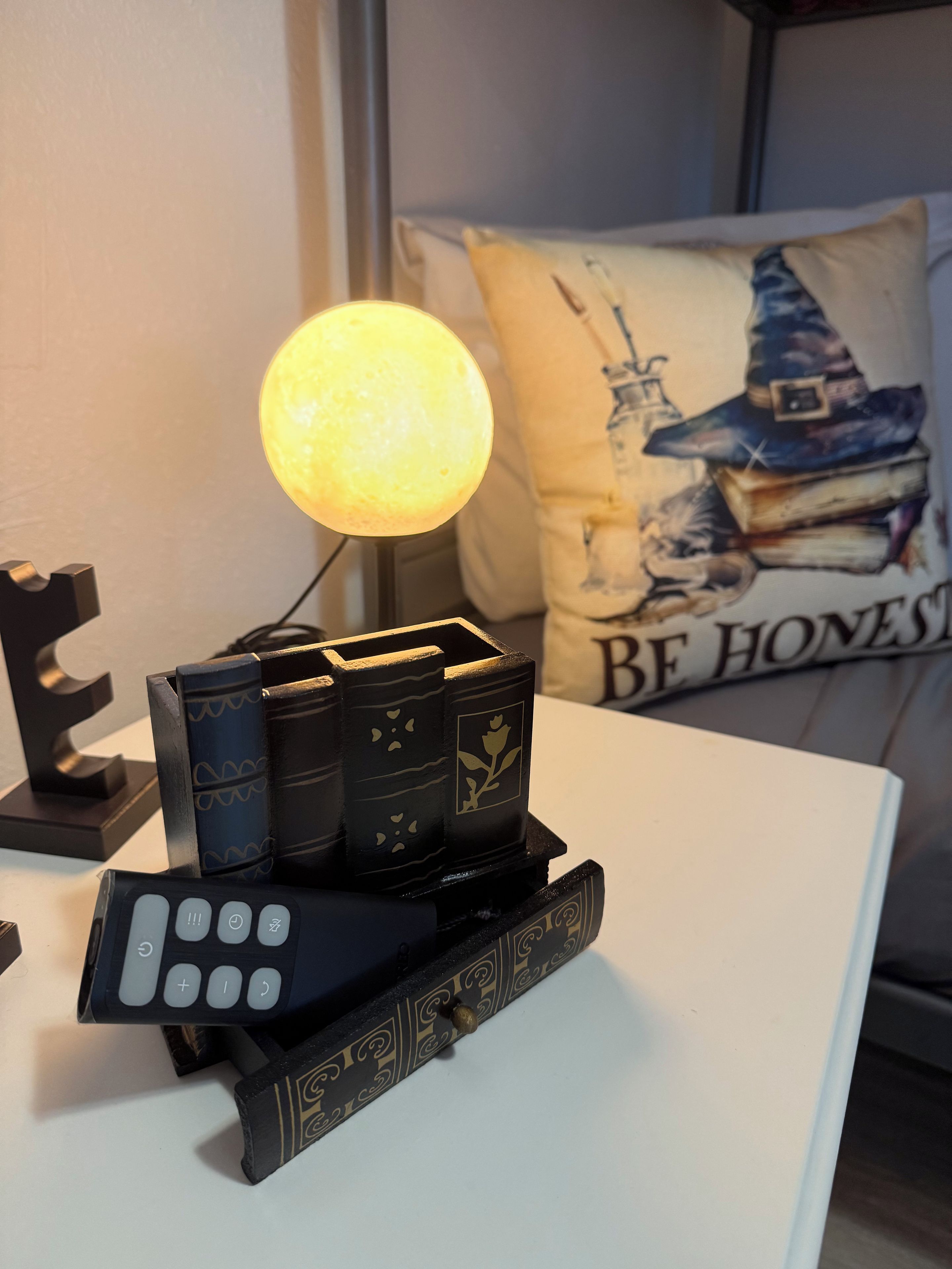 Una mesa con una lámpara, libros y un control remoto.
