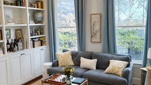 A living room with a grey sofa, a bookshelf, and a coffee table with books. - Upscale 5BR House in Morningside – Perfect for World Cup Groups (Atlanta)